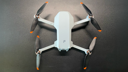 Overhead view of a compact white and gray drone with four propellers, displayed on a dark textured surface.