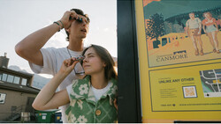 Two people sharing ice cream cones outdoors on a city street, with one person adjusting their sunglasses.