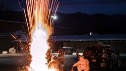 Pyrotechnic explosion with orange sparks shooting upward during nighttime fire training exercise.