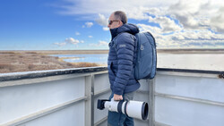 Birdwatcher with telephoto lens and backpack observing wetlands from an observation platform.