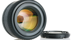 Camera lens with amber-tinted glass elements and detached rear cap on white surface.