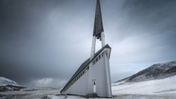 Modern white chapel with tall spire tilted dramatically in snowy Arctic landscape under stormy sky.