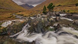 Mountain stream with smooth, flowing water cascading over layered rock formations in a misty valley.