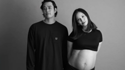 Black and white portrait of a man and pregnant woman standing together against a neutral background.