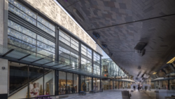 Modern transit station with expansive skylights, retail storefronts, and geometric ceiling architecture.