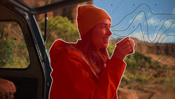 Person in red jacket and beanie leaning out of vehicle window against desert landscape.