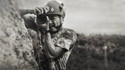Climber in helmet peers through camera lens while secured to rock wall.