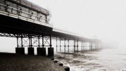 Pier structure receding into thick fog with dark metal framework and support pillars extending into turbulent water.