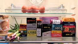 Refrigerator shelf displaying vintage film stock boxes and fresh produce including apples and vegetables.
