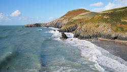 Rocky coastal cliffs with turquoise water and breaking waves beneath grassy headland.