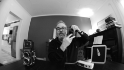 Photographer holding a rangefinder camera in a black and white self-portrait taken with a wide-angle lens.