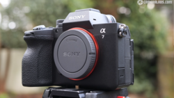 Sony α7 mirrorless camera body mounted on tripod with blurred foliage background.