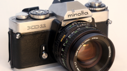Minolta XD11 film SLR camera with black leather grip and attached prime lens.