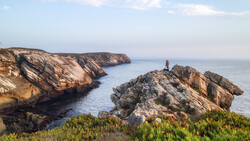 Rugged coastal cliffs with golden-hour sunlight illuminating rocky outcrops and a solitary sea stack.