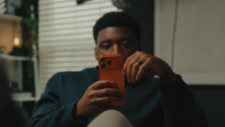 Man holding an orange smartphone up to his face while looking at the screen.