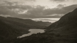 Mountain valley landscape with winding river and dramatic cloudy sky in monochrome.