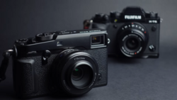Three rangefinder cameras arranged on a gray surface with selective focus on the nearest black camera.