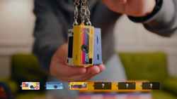 Person holding a yellow and pink instant camera pendant on a chain.