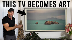 Man in black polo shirt pointing to framed landscape photo displaying turquoise water and rocky islands.