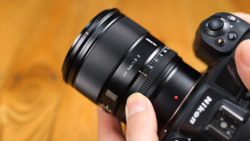 Close-up of a camera lens being held and adjusted by hand against a warm golden background.