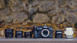 Olympus OM camera body with five interchangeable lenses arranged in a product lineup.