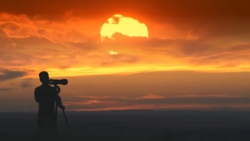 Silhouetted photographer with telephoto lens on tripod shooting a massive golden sunset.