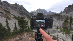 Camera mounted on tripod displaying mountain valley landscape on its rear screen.