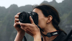 Photographer with Canon camera capturing landscape with dramatic mountain peaks in background.