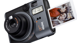 Instax hybrid instant camera with built-in flash and control dial, ejecting a printed photograph showing two people.