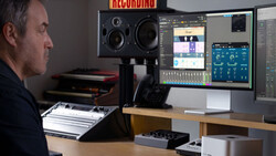 Music producer working at a recording studio desk with studio monitors, audio interface, and dual monitors displaying DAW software.