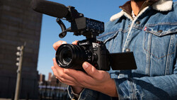 Videographer holding a cinema camera with an external monitor and microphone mounted on an urban rooftop.