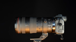 Telephoto lens mounted on mirrorless camera body against black background, side view.
