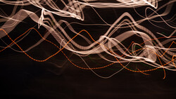 Light painting photograph with flowing curves of orange and white light trails against black background.