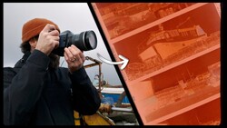 Photographer holding DSLR camera with telephoto lens, wearing brown beanie and dark jacket, positioned in front of orange industrial structure.