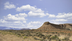 Distinctive cone-shaped butte rising from arid desert landscape under partly cloudy sky.