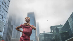 Woman in burgundy dress posing against urban skyline with tall buildings obscured by fog.