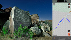 Memorial stone with engraved text positioned among large boulders under clear blue sky.