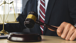 Attorney in business suit holding a gavel above its sound block, with scales of justice visible on desk.