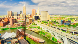 Aerial view of a Midwest city skyline with downtown towers reflected in a river bend.