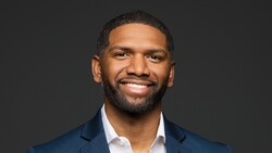 Professional headshot of a man wearing a dark blue blazer and white dress shirt against a dark gray background.