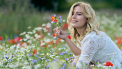 Woman with blonde wavy hair holding colorful wildflowers in a blooming meadow.