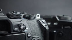 Close-up of professional camera body showing AEL/AFL and INFO buttons with textured grip in sharp focus, background blurred.
