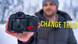 Photographer holding mirrorless camera with LCD screen displaying menu settings in snowy outdoor environment.