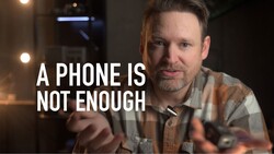 Man in plaid shirt gesturing while speaking, with text overlay reading "A PHONE IS NOT ENOUGH."