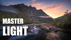 Mountain landscape at sunset with a flowing river in the foreground and dramatic sky.