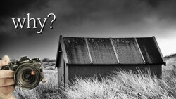 Photographer holding a DSLR camera pointed at a derelict house with solar panels in an overgrown field.