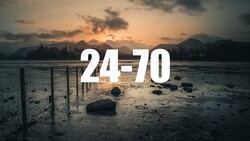 Mudflats at sunset with wooden posts and boulders scattered across wet sand, mountains silhouetted against golden sky.