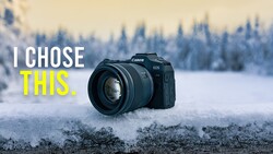 Canon EOS camera with lens on snow-covered ground, evergreen forest in background.