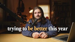 Podcaster speaking into a microphone at a desk with a laptop, shot in warm studio lighting.