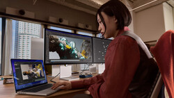 Video editor working on color grading with dual monitors in a bright studio workspace.